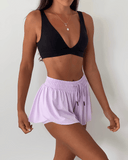 Person wearing a black sports bra and light purple shorts on a plain background