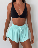 Person wearing a black sports bra and pale green shorts on a plain background