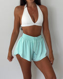 Woman wearing a white sports bra and light blue shorts against a plain background