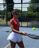 Woman playing paddle tennis on a court with trees and a fence in the background.